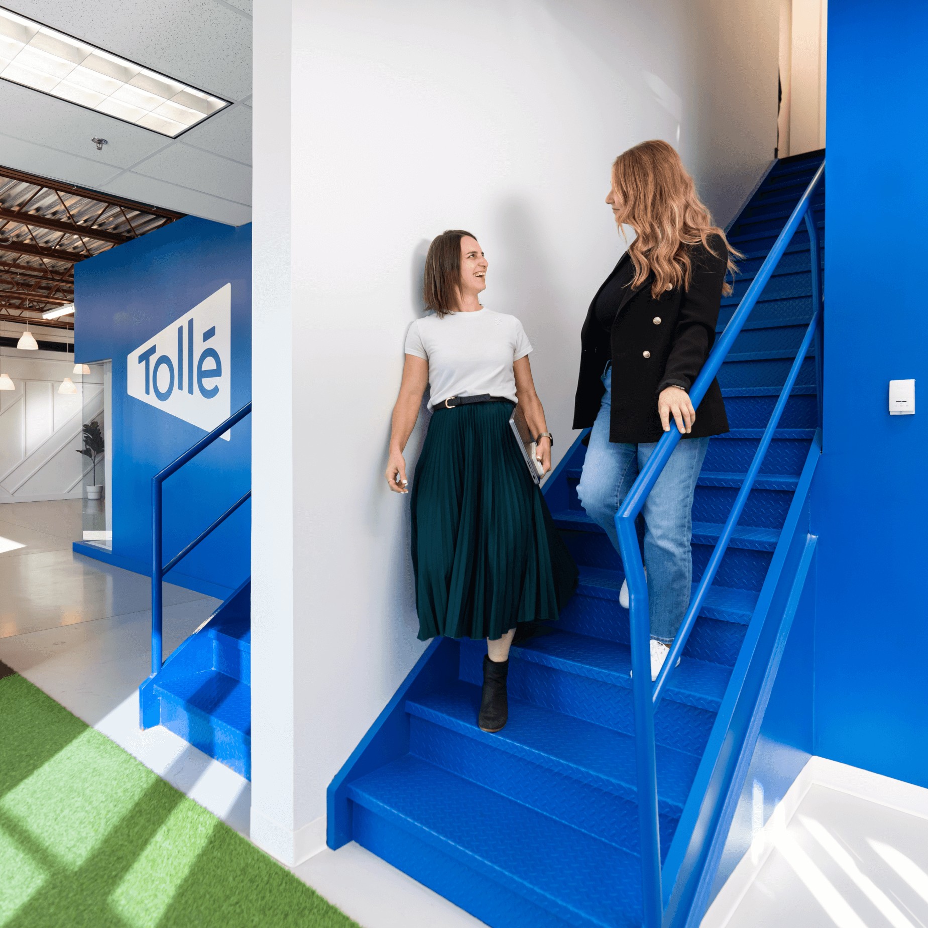 Karine Desrosiers et Jessica Filion Pion en conversation dans les escaliers, avec le logo de Tollé sur un mur en arrière-plan.