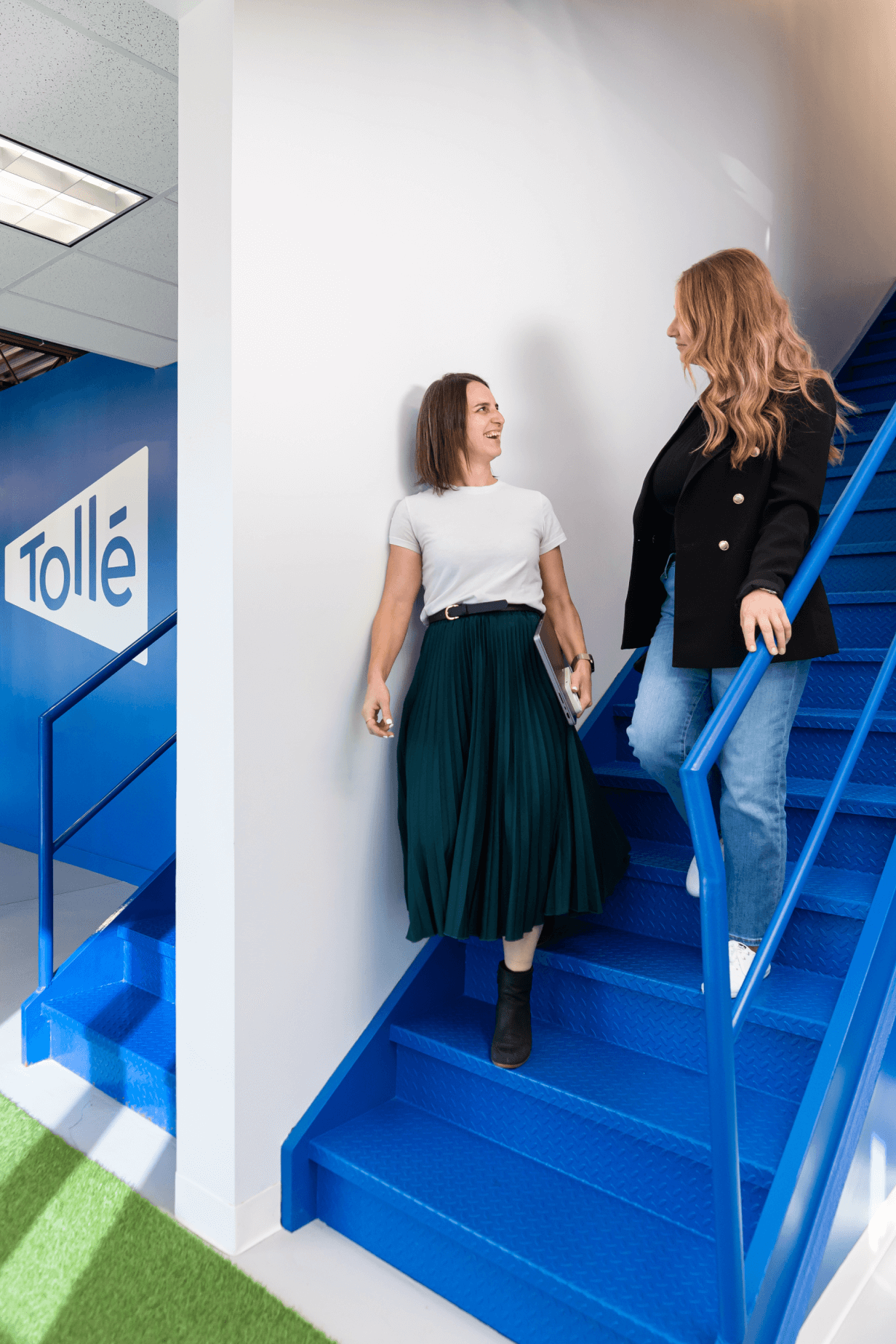 Karine Desrosiers et Jessica Filion Pion en conversation dans les escaliers, avec le logo de Tollé sur un mur en arrière-plan.